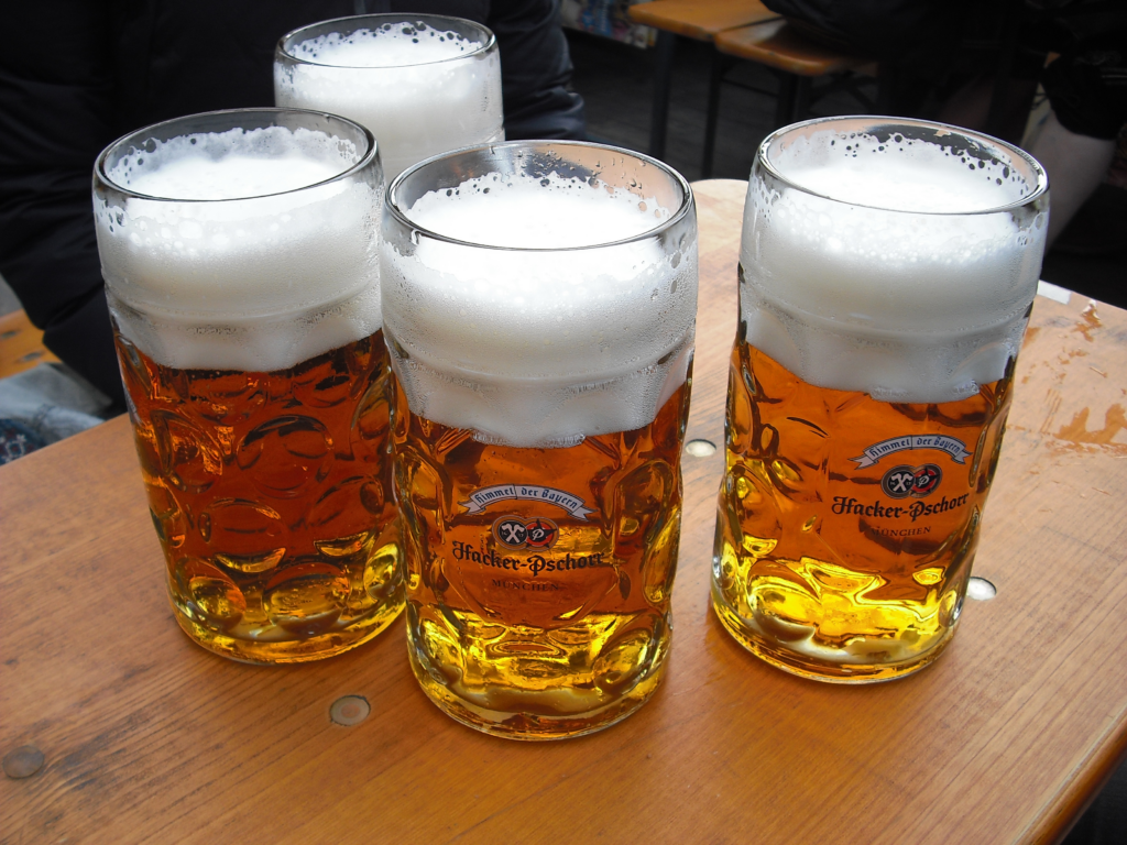 Imagem de quatro cervejas alemãs em copos grandes de vidro em cima de uma mesa